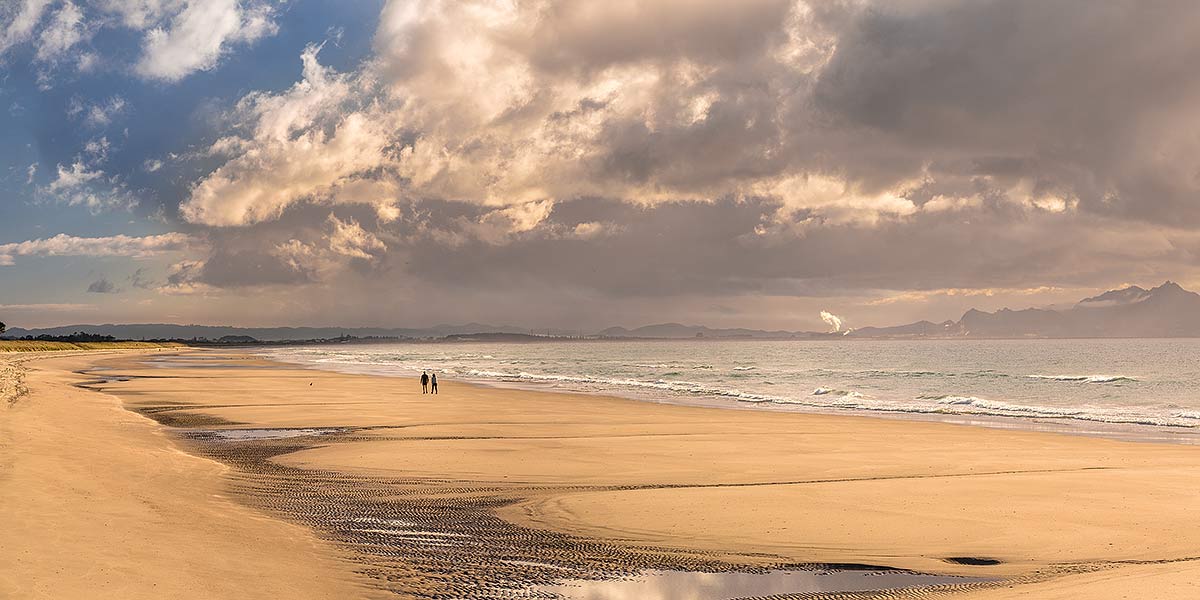 Image of Ruakaka Beach panorama, with people walking in evening light. Mt Manaia (right, 420m) behind right, at the Whangarei Harbour Heads, Ruakaka, Whangarei District, Northland Region, New Zealand (NZ) stock photo image