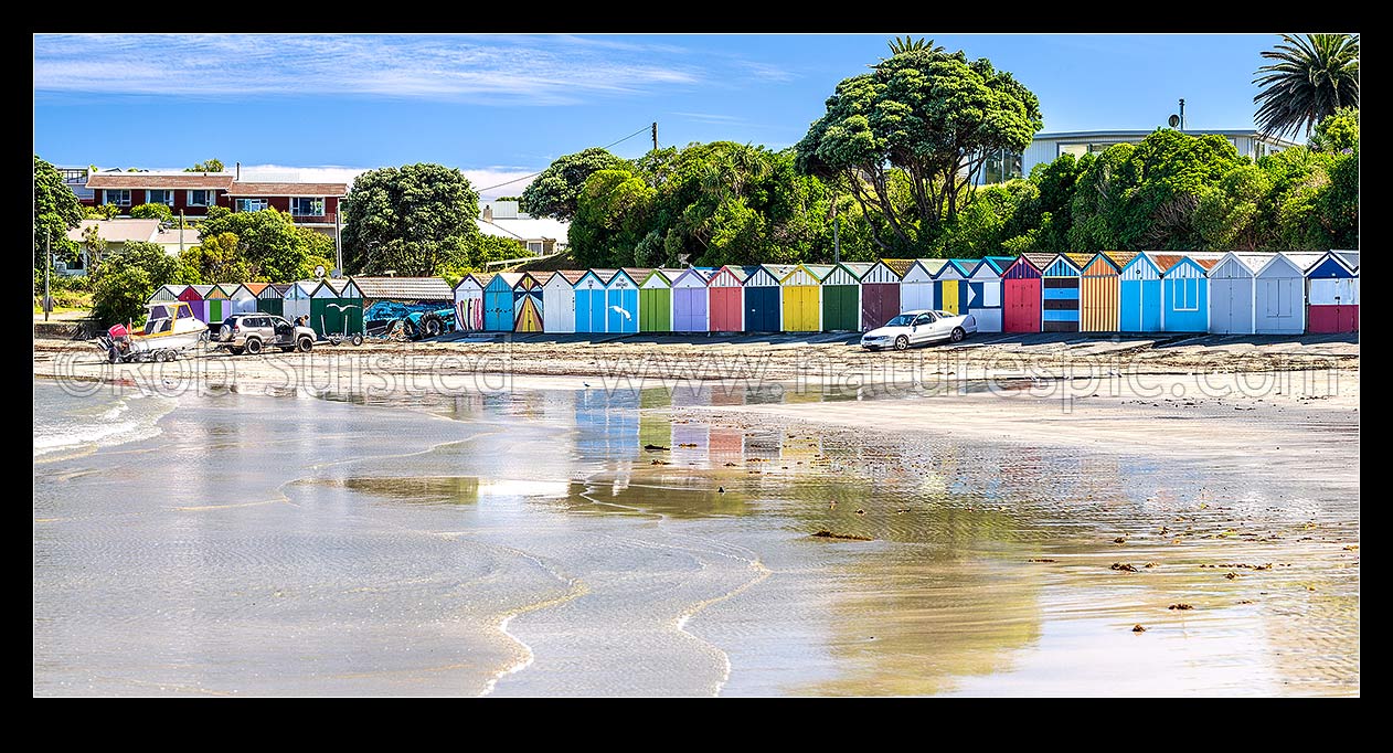 Image of Titahi Bay boatsheds, iconic brightly painted sheds on Titahi Bay beach front, north end, with boat about to be launched. Panorama, Titahi Bay, Porirua City District, Wellington Region, New Zealand (NZ) stock photo image