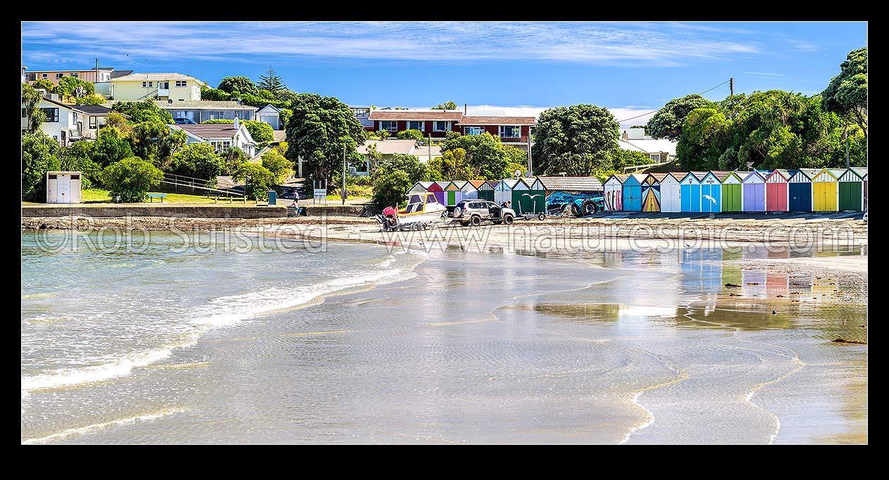 Image of Titahi Bay boatsheds, iconic brightly painted sheds on Titahi Bay beach front, north end, with boat about to be launched. Panorama, Titahi Bay, Porirua City District, Wellington Region, New Zealand (NZ) stock photo image