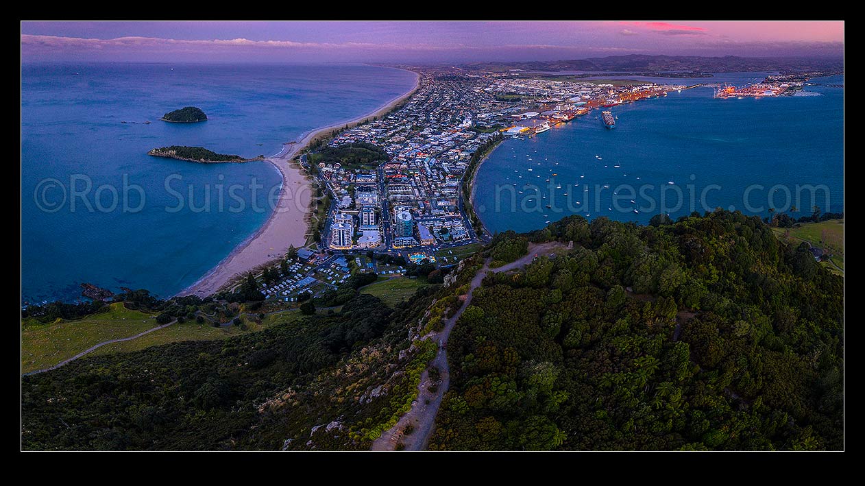 Image of Mt Maunganui, or Mauao, at the Tauranga Harbour Entrance. 231m high lava dome. Moturiki Island at left, Tauranga Port cenre, City right. Aerial panorama at dusk, Mount Maunganui, Tauranga District, Bay of Plenty Region, New Zealand (NZ) stock photo image