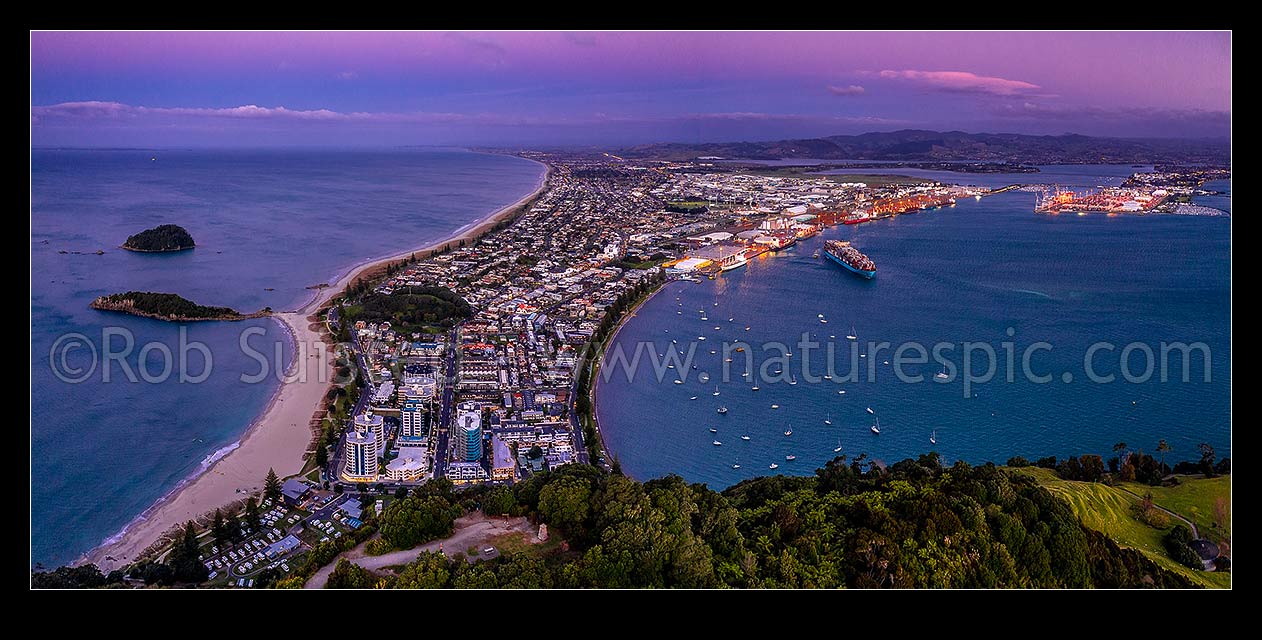 Image of Mt Maunganui, or Mauao, at the Tauranga Harbour Entrance. 231m high lava dome. Moturiki Island at left, Tauranga Port cenre, City right. Aerial panorama at dusk, Mount Maunganui, Tauranga District, Bay of Plenty Region, New Zealand (NZ) stock photo image