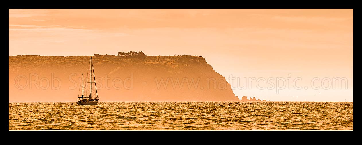 Image of Sailboat silhouette at Mana Island on a hazy summer evening sunset. Panorama, Titahi Bay, Porirua City District, Wellington Region, New Zealand (NZ) stock photo image