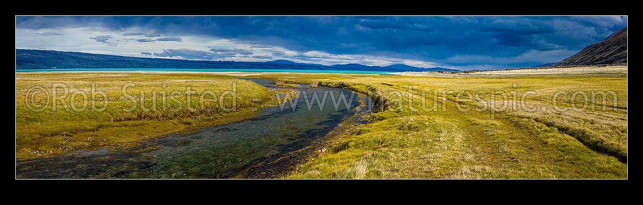 Image of Lake Pukaki's turquoise blue waters against a heavy moody sky. Lake Pukaki lake shore and edge in the Tasman Valley where a spring fed creek passes. Panorama, Lake Pukaki, MacKenzie District, Canterbury Region, New Zealand (NZ) stock photo image