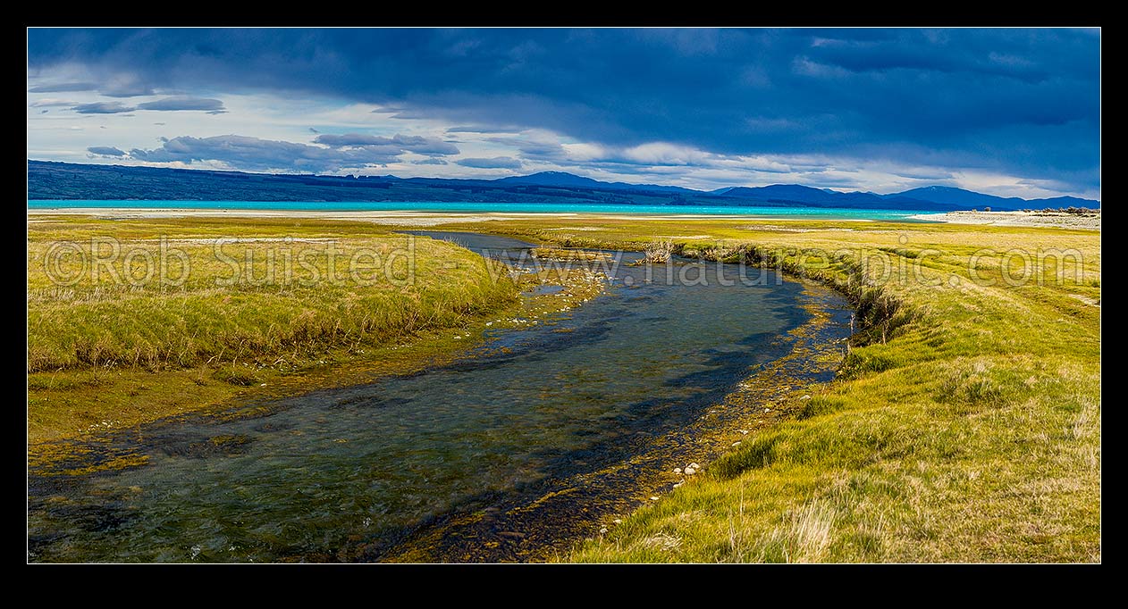 Image of Lake Pukaki's turquoise blue waters against a heavy moody sky. Lake Pukaki lake shore and edge in the Tasman Valley where a spring fed creek passes. Panorama, Lake Pukaki, MacKenzie District, Canterbury Region, New Zealand (NZ) stock photo image