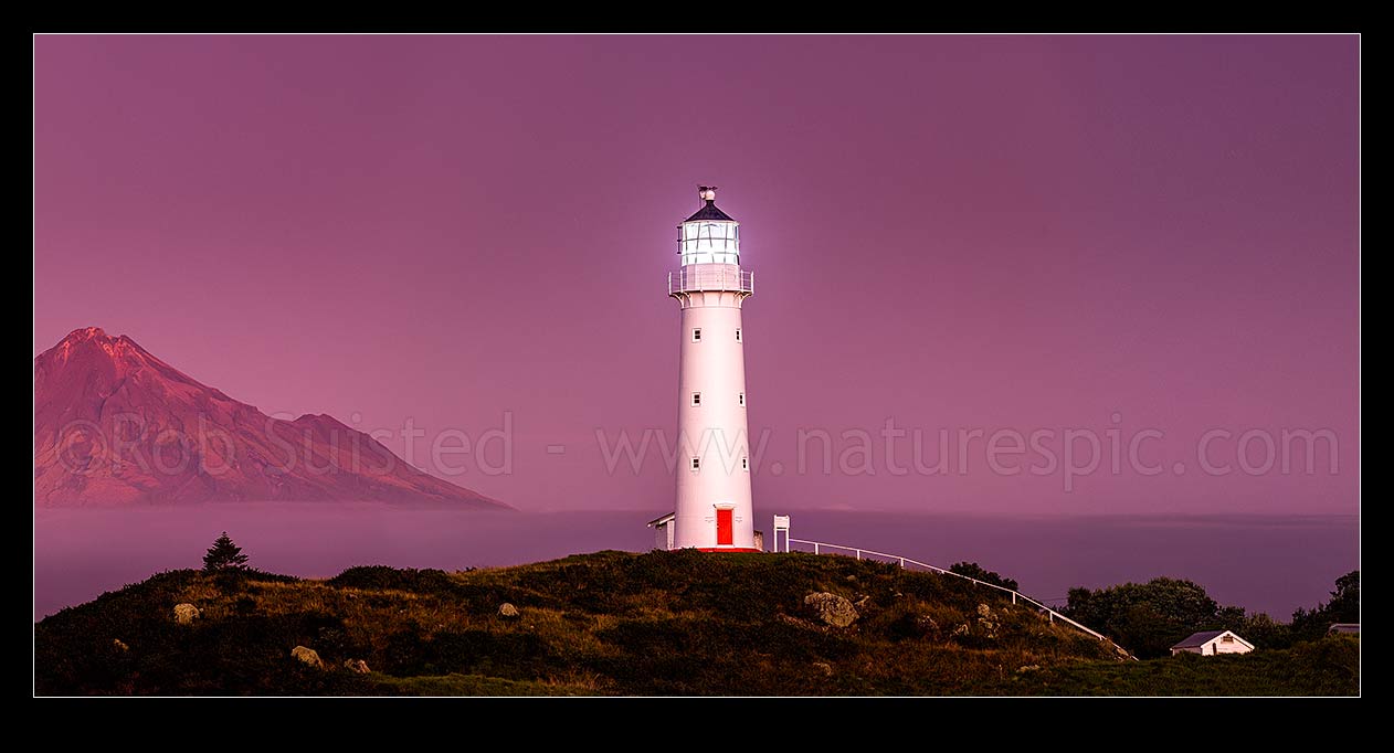 Image of Cape Egmont lighthouse with Mount Taranaki (2518m) and Egmont National Park behind, in the post dusk twilight. Panorama, Cape Egmont, South Taranaki District, Taranaki Region, New Zealand (NZ) stock photo image