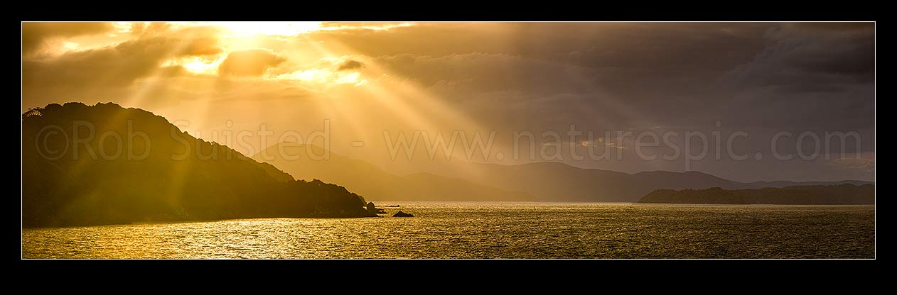 Image of Sunlit rays over Paterson Inlet Whaka a Te Wera. Evening crepusular rays and glowing skies lighting Ulva Island at left. Rakiura panorama, Paterson Inlet, Stewart Island District, Southland Region, New Zealand (NZ) stock photo image