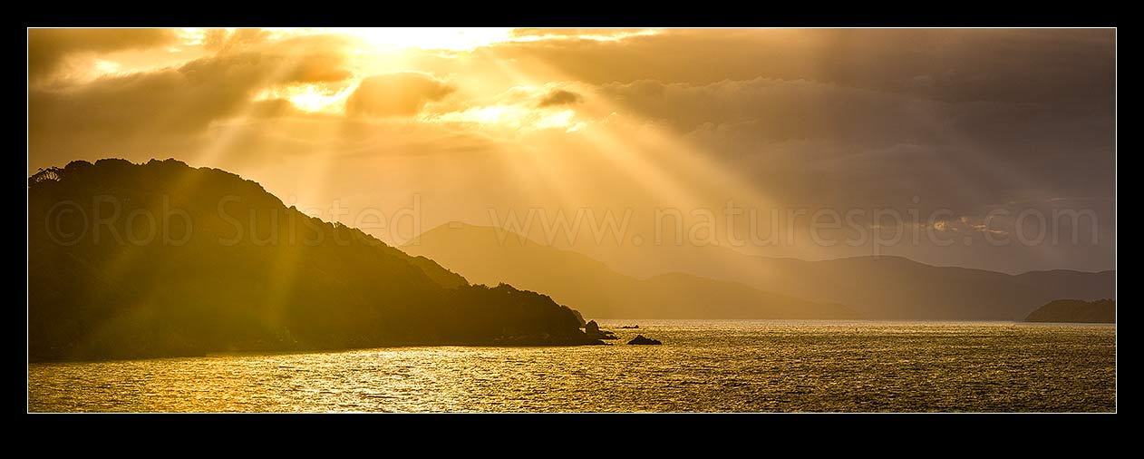 Image of Sunlit rays over Paterson Inlet Whaka a Te Wera. Evening crepusular rays and glowing skies lighting Ulva Island at left. Rakiura panorama, Paterson Inlet, Stewart Island District, Southland Region, New Zealand (NZ) stock photo image