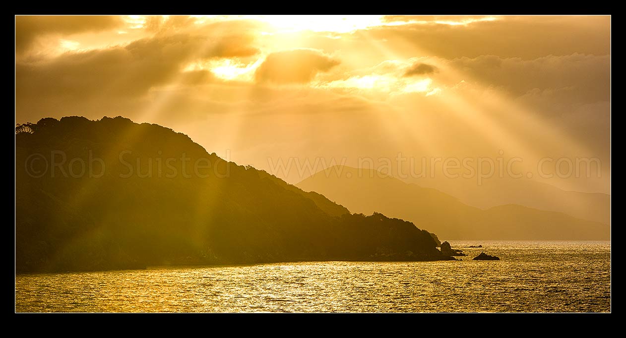 Image of Sunlit rays over Paterson Inlet Whaka a Te Wera. Evening crepusular rays and glowing skies lighting Ulva Island at left. Rakiura panorama, Paterson Inlet, Stewart Island District, Southland Region, New Zealand (NZ) stock photo image