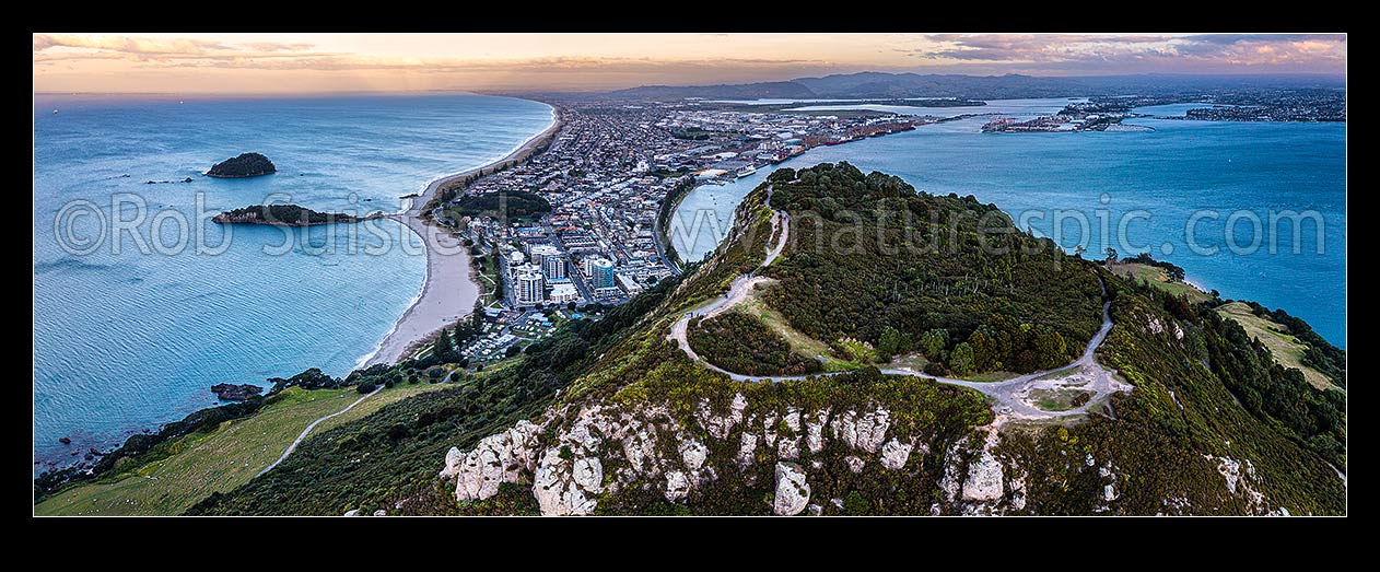 Image of Mt Maunganui summit Mauao at the Tauranga Harbour Entrance. 231m high lava dome. Mt Maunganui Beach left, Tauranga Harbour right. Aerial panorama at dusk, Mount Maunganui, Tauranga District, Bay of Plenty Region, New Zealand (NZ) stock photo image